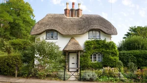 Quaint English thatched cottage with ivy-covered walls and blooming front garden.