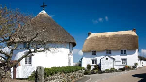 Whitewashed round and square thatched cottages under bright blue sky in Cornwall village.