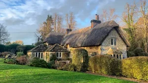 Charming thatched cottage in the English countryside with manicured garden and stone walls.
