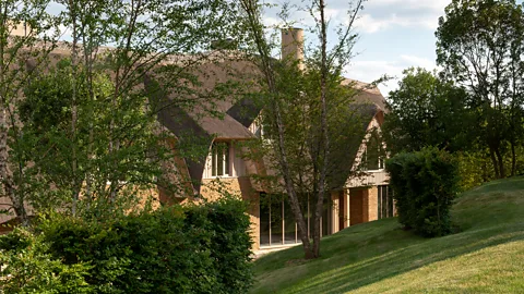 Modern thatched cottage surrounded by trees and rolling hills in the British countryside